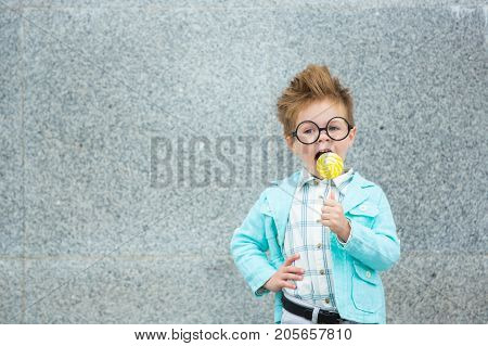 Fashion baby boy in mint jacket stands on a gray wall background. Trendy boy with lollipop standing on the street.