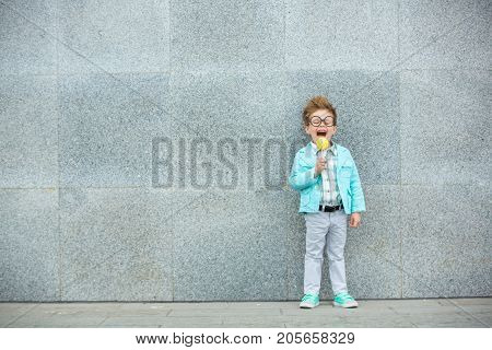Fashion baby boy in mint jacket and sneakers stands on a gray wall background. Trendy boy with lollipop standing on the street.