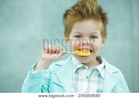 Fashion baby boy in mint jacket and sneakers stands on a gray wall background. Trendy boy with lollipop standing on the street.