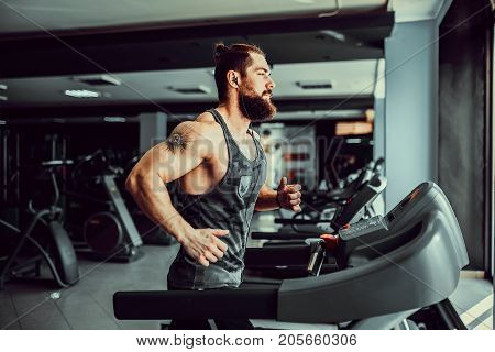 Fit Muscle Bearded Man With Headphones Running on Treadmill in Gym.
