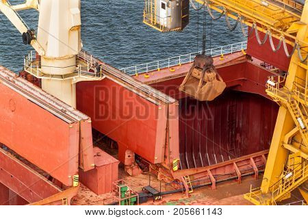 Crane unloads iron ore at the harbor. Trade in raw materials. Work at a port in the Baltic Sea