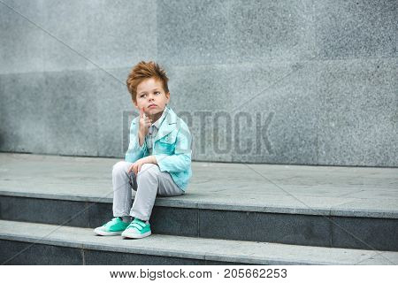 Fashion baby boy in mint jacket and sneakers posing on a gray wall background. Trendy boy standing on the street.