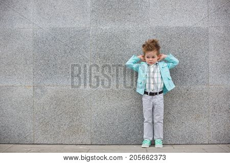 Fashion baby boy in mint jacket and sneakers posing on a gray wall background. Trendy boy standing on the street.