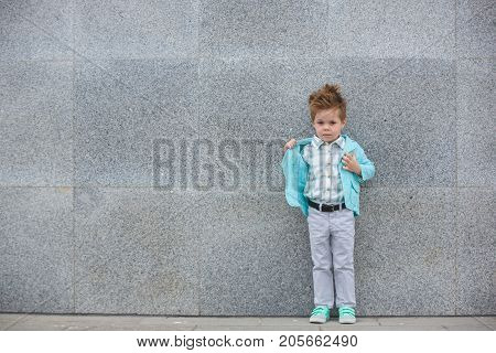 Fashion baby boy in mint jacket and sneakers posing on a gray wall background. Trendy boy standing on the street.