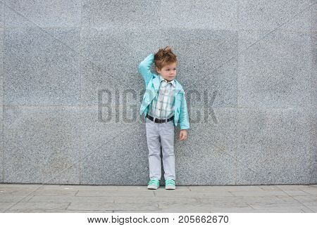 Fashion baby boy in mint jacket and sneakers posing on a gray wall background. Trendy boy standing on the street.
