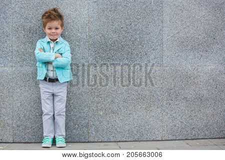 Fashion baby boy in mint jacket and sneakers posing on a gray wall background. Trendy boy standing on the street.