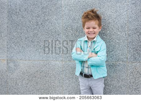 Fashion baby boy in mint jacket posing on a gray wall background. Trendy boy standing on the street.
