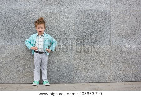 Fashion baby boy in mint jacket and sneakers posing on a gray wall background. Trendy boy standing on the street.