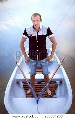 handsome man standing in the white boat, happy teenager in light shorts and shirt, young guy enjoys outdoor recreation
