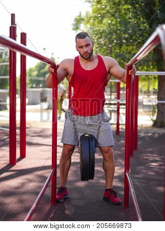 A strong man with sexy body is doing exercises on his feet. A handsome young man lifts weights with his feet in the park.