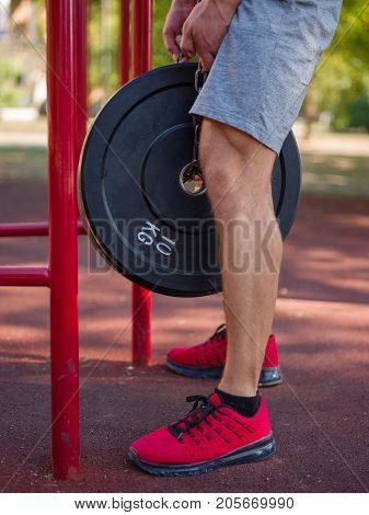 A strong man with sexy body is doing exercises on his feet. A handsome young man lifts weights with his feet in the park.