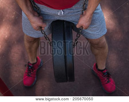 A strong man with sexy body is doing exercises on his feet. A handsome young man lifts weights with his feet in the park.