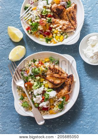 Yogurt marinated grilled chicken breast and israeli couscous and vegetables tabouli salad on a blue background top view