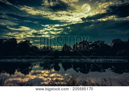 Sky With Many Star And Full Moon Above Silhouettes Of Trees And Lake.
