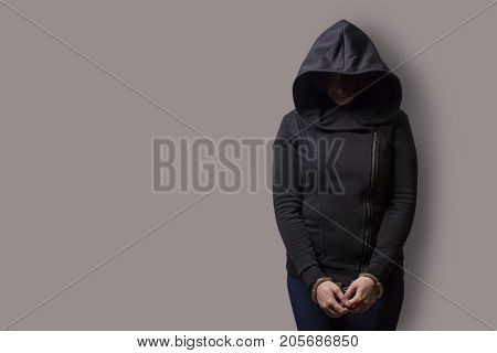 front view of a girl in a black hood with handcuffed hands isolated on a gray