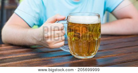 Hand holding a glass of beer on wooden table.