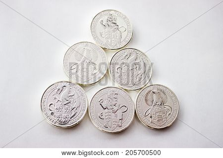 On a gray background are silver coins of an investment silver from a British mints. Dragon of Wales Lion of England and Griffin of Edward III.