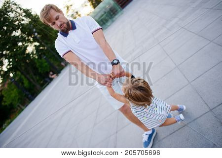 Young dad is playing with a charming little daughter. The man is holding the baby by the handles.. The child rejoices.