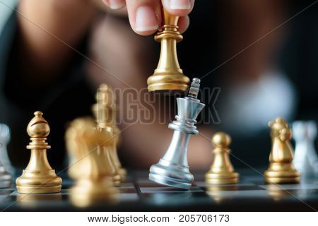 Close up shot hand of business woman moving golden chess to defeat and kill silver king chess on white and black chess board for business challenge competition winner and loser concept selective focus on king chess shallow depth of field