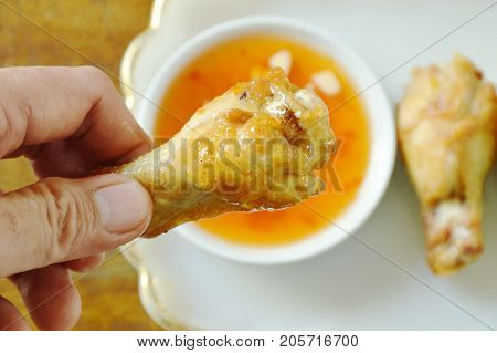 hand picking fried chicken drumsticks with salt and pepper dipping sweet chili sauce to eating