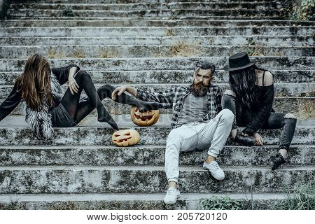Halloween jack o lantern symbols. People or friends on stony stairs. Bearded man sitting with girls. Women with pumpkin heads. Halloween holiday celebration concept.
