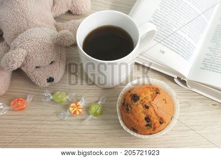 Leisure. A cup of coffee a cupcake and a book on the table.