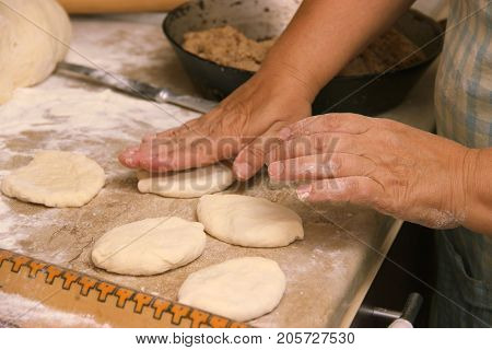 Senior woman baking pies in her home kitchen.Grandma cooks pies. Home cooked food. omemade mold cakes of the dough in the women's hands. The process of making pie dough by hand.