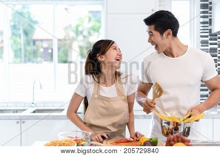 Young asian woman cutting slice vegetables making salad heathy food with fruits and man cooking menu for dinner in kitchen at home couple together romantic