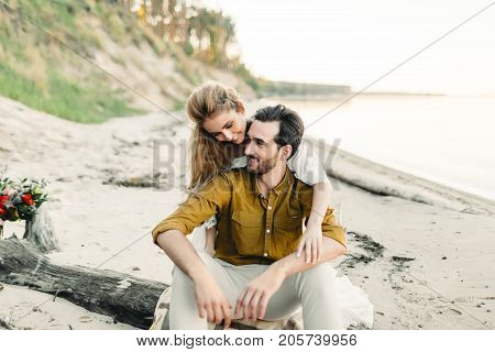 A young couple is having fun and hugging on the beach. Beautiful girl embrace her boyfriend from back. Wedding walk. A newlyweds looks at each other. Artwork, soft focus