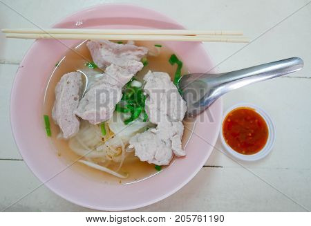 Traditional food Thai style noodle mince pork in bowl spoon and chopsticks with Spicy sauce. on white wooden table.
