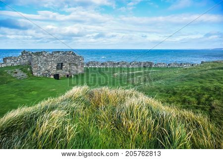 The remains of Peel Castle's wall on top of Peel hill covered with green grass on the ground, Isle of Man