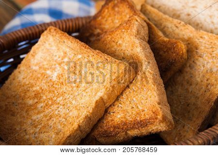 Breakfast background, white bread toasts in wicker breadbasket on checkered table napkin half covering wooden table, closeup, vertical