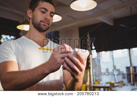 Young waiter taking order while standing in cafe