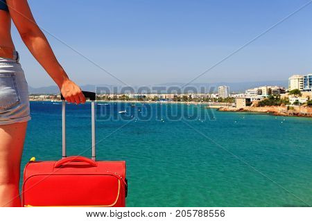Woman with red suitcase close-up. Girl with suitcase against mediterranean sea background. Traveling background with copy space on emerald sea water backdrop.