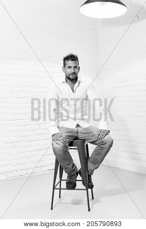 Black and white full length indoor portrait of handsome man in casual cloth sitting on barstool.