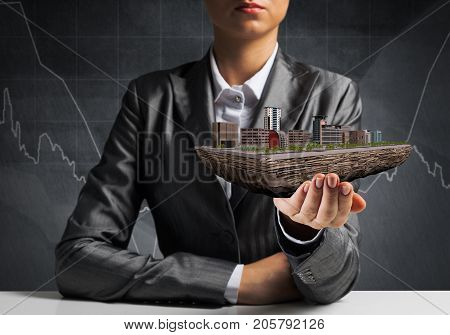 Cropped image of businessman in suit presenting in his hand modern city block with business sketches on background. 3D rendering.