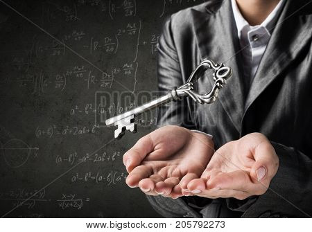 Cropped image of businessman in suit keeping big key in hands with business sketches on dark wall on background.