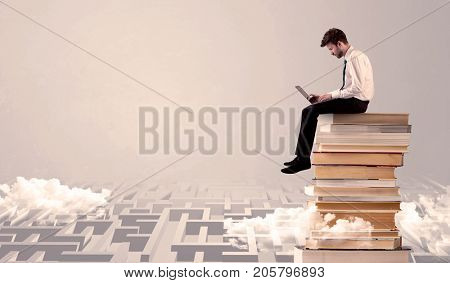 A businessman with laptop tablet in elegant suit sitting on a stack of books on top of sandy labirynth background concept