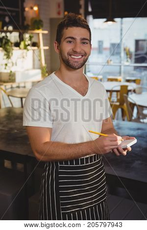 Portrait of happy waiter taking order by counter at cafe