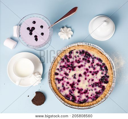 Comfort food. Blueberry open pie served with milk smoothie marshmellows and cookie on pale blue table above view