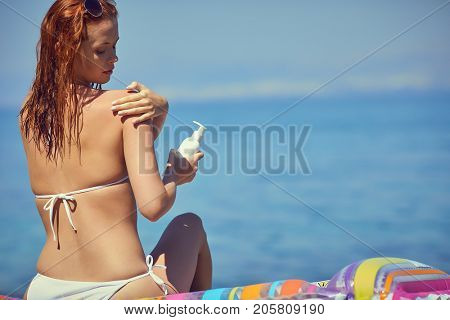 Girl in bikini applying sun lotion at seaside
