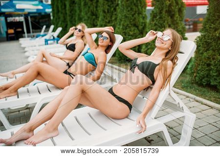 Three slim girls relax on deck chairs outdoors