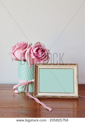 Pink roses in a mint enamel vase with an antique frame with gold decor against neutral painted wall. Shabby chic country style. Space for text