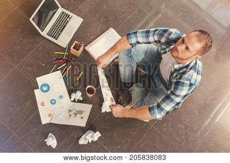 Lack of ideas. Top view on a young startupper in casual sitting on the floor and looking into vacancy while struggling with business project implementation.