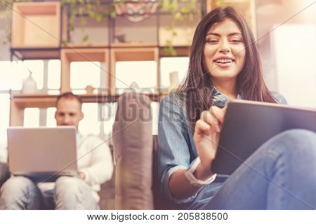 Young business generation. Low angle shot of a beaming young businesswoman in casual surfing internet on her digital tablet while sitting on a sofa and working next to a male colleague