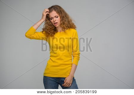 beautiful curly young woman in yellow clothes clings to one's head for vexation on a gray background