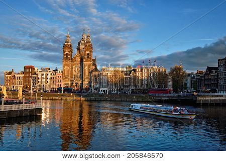 AMSTERDAM, NETHERLANDS - MAY 9, 2017: Tourist boat in Amsterdam canal and Church of Saint Nicholas (Sint-Nicolaaskerk) on sunset. Amsterdam, Netherlands