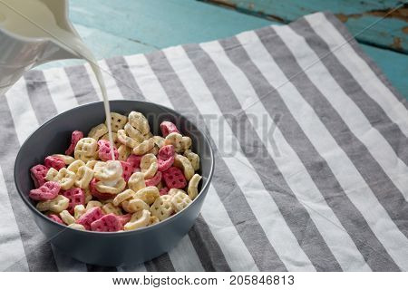 Pouring milk into bowl of honeycomb cereal on white background