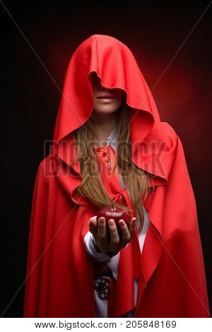beautiful woman with res cloack holding red apple in studio