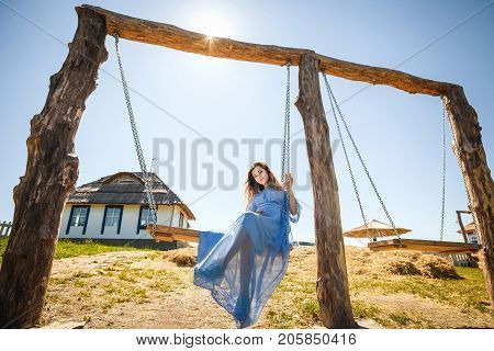 happy young girl sitting on swing, pretty woman in blue dress have resting in village